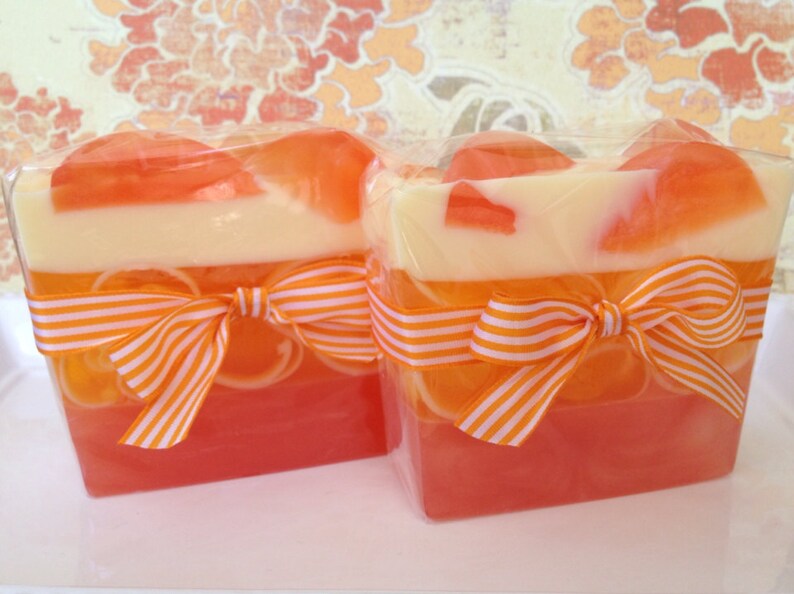 May include: Two rectangular bars of layered soap with orange, white, and pink colors. Each bar is tied with an orange and white striped ribbon.