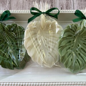 Pode incluir: Tr&ecirc;s sabonetes em forma de folha, verde e branco, embrulhados em pl&aacute;stico transparente com la&ccedil;os de fita verde.