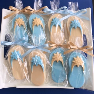 May include: Flip-flop shaped cookies, individually wrapped in clear cellophane and tied with satin ribbons. The cookies are light blue and tan, with a starburst design on the straps. The ribbons are light blue and tan.