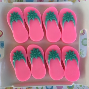 May include: Eight pink flip-flops with teal straps and a teal flower design on the top. The flip-flops are arranged in two rows of four inside a white tray.