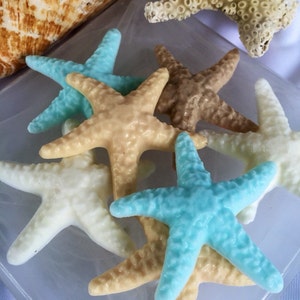 May include: A collection of five starfish soap bars in various colors, including light blue, beige, and white. The soaps are arranged on a white surface.