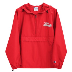 May include: Red Champion brand windbreaker jacket with a zipper closure and a gray embroidered image of a vehicle with a roof rack on the front. The jacket has a hood and a pouch pocket on the front.