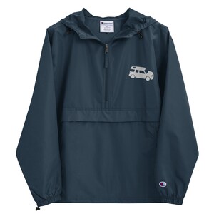 May include: A navy blue Champion windbreaker jacket with a zipper closure and a white graphic of a camper van on the front. The jacket has a hood and a kangaroo pocket.