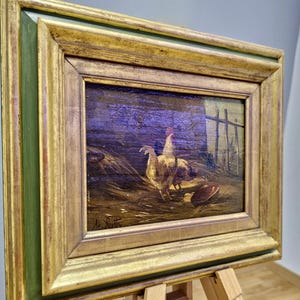 Peut inclure: Peinture &agrave; l'huile de poulets dans un cadre dor&eacute; et vert orn&eacute;. L'&oelig;uvre repr&eacute;sente deux poulets dans une cour de ferme avec une cl&ocirc;ture en arri&egrave;re-plan. La peinture est sign&eacute;e dans le coin inf&eacute;rieur gauche.