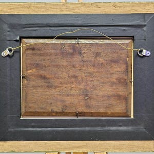 Peut inclure: Dos d'une &oelig;uvre encadr&eacute;e. Le cadre est en bois clair avec un bord noir. L'&oelig;uvre elle-m&ecirc;me est de couleur bois fonc&eacute;. Un fil est tendu &agrave; l'arri&egrave;re pour l'accrochage. Du mat&eacute;riel m&eacute;tallique est fix&eacute; au cadre.
