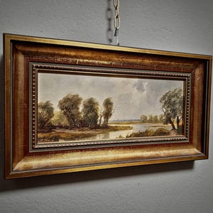 Beautifully crafted original oil painting showcasing a quiet European landscape, this vintage framed artwork is perfect for nature wall decor and mid-century rustic interiors. The textured brushwork and horizontal format offer balance and calm, while the signed panel makes it a piece of collectible fine art. A lovely gift idea for art collectors, homeowners, or those seeking German vintage artwork with history and charm. Includes keywords like Dark, Moody, and mid-century modern.