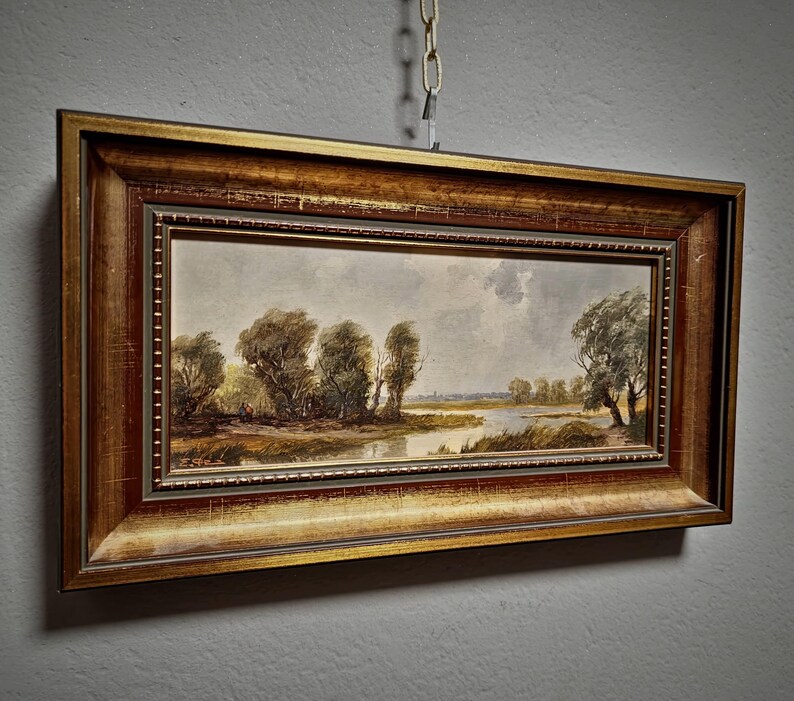 Beautifully crafted original oil painting showcasing a quiet European landscape, this vintage framed artwork is perfect for nature wall decor and mid-century rustic interiors. The textured brushwork and horizontal format offer balance and calm, while the signed panel makes it a piece of collectible fine art. A lovely gift idea for art collectors, homeowners, or those seeking German vintage artwork with history and charm. Includes keywords like Dark, Moody, and mid-century modern.