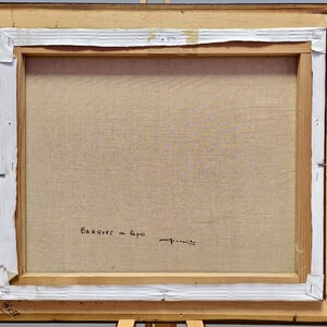 May include: The back of a framed painting with a wooden frame. The canvas is stretched and stapled to the frame. The text "BARQUES au Repos" is written in black ink, along with a signature. The dimensions are 38 x 46 inches.