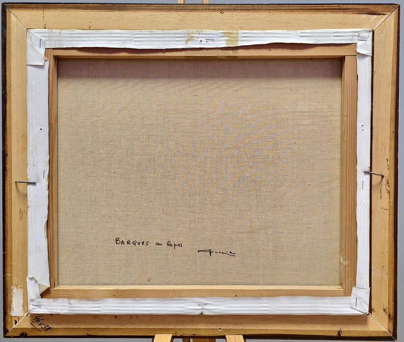 May include: The back of a framed painting with a wooden frame. The canvas is stretched and stapled to the frame. The text "BARQUES au Repos" is written in black ink, along with a signature. The dimensions are 38 x 46 inches.