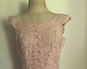 May include: A pink lace and linen dress with a fitted bodice and a full skirt. The dress has a scoop neckline and cap sleeves.