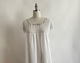 Puede incluir: Un camisón blanco de algodón con un ribete de encaje de ganchillo alrededor del escote y mangas cortas.
