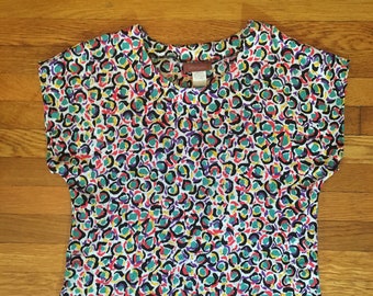 May include: A white short-sleeved shirt with a colorful abstract print of circles and dots in shades of red, yellow, green, blue, and purple.
