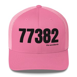 Può includere: Cappellino da camionista rosa e nero con il numero 77382 e il testo "the woodlands" sul davanti.