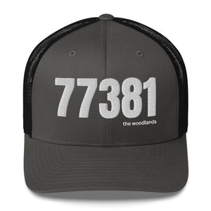 May include: A dark gray and black trucker hat with a white embroidered number "77381" and the text "the woodlands" below the number.