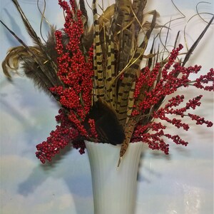 May include: A white ceramic vase with a fluted design holds a bouquet of red berries and brown pheasant feathers.
