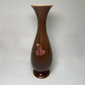 May include: A brown ceramic vase with a flared top and a rounded base. The vase has a glossy finish and a Red Wing Pottery sticker. The vase is approximately 8 inches tall.