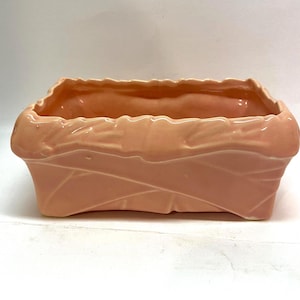 May include: A pale pink ceramic planter with a woven design. The planter is rectangular and has a slightly rounded rim.