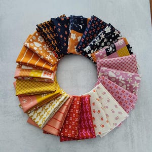 Peut inclure: Disposition circulaire de carrés de tissu pliés de différentes couleurs et motifs. Les tissus comprennent des motifs floraux, géométriques et abstraits dans des tons d'orange, de jaune, de rose, de rouge et de bleu marine. Les tissus sont disposés sur une surface gris clair.