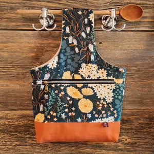 May include: A dark green tote bag with a floral print featuring white and yellow flowers. The bag has a zipped pocket and a brown bottom.