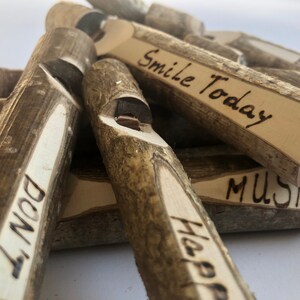May include: A collection of wooden whistles with various messages burned into the wood, including "Smile Today", "Music", "Happy", "Don't", and "Enjoy".