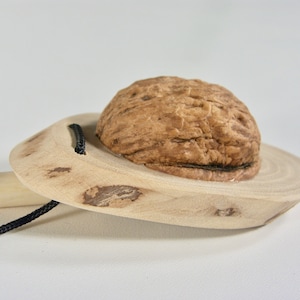May include: A handmade wooden nutcracker with a natural walnut shell. The nutcracker has a light-colored wooden base with a small handle and a black cord. The walnut sits in a circular indentation.