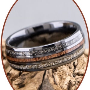 Op de afbeelding: Een zwarte ring van wolfraamcarbide met een houten inlay en een zilverkleurige band. De ring ligt op een stuk hout.