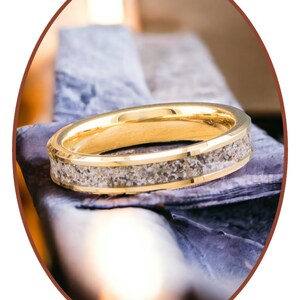 Op de afbeelding: Een gouden ring met een band van zand ingebed in het metaal.