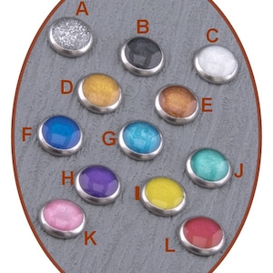 Op de afbeelding: Twaalf ronde, metalen, decoratieve knoppen met verschillende gekleurde epoxyharsinzetstukken. De knoppen zijn in een cirkel op een grijze achtergrond gerangschikt. De kleuren omvatten zilver, zwart, wit, goud, blauw, turquoise, paars, geel, roze en rood.