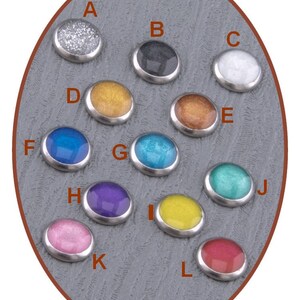 May include: Assortment of 12 round, metallic, decorative buttons with various colors and finishes. The buttons are arranged in a circle on a gray background.