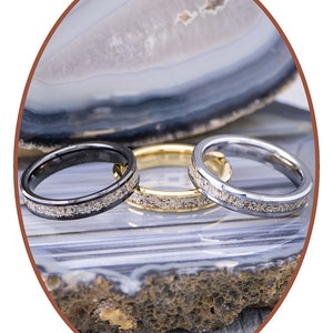 Op de afbeelding: Drie ringen van wolfraamcarbide met een zwarte, gouden en zilveren afwerking. Elke ring heeft een dunne lijn van ingebedde zilveren deeltjes.