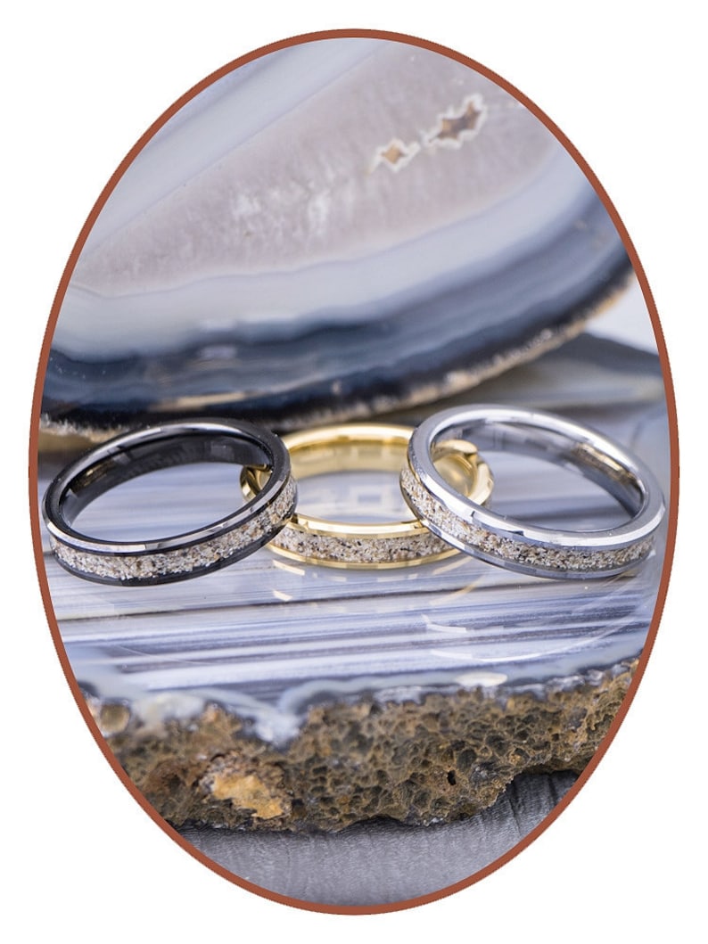 Op de afbeelding: Drie ringen van wolfraamcarbide met een zwarte, gouden en zilveren afwerking. Elke ring heeft een dunne lijn van ingebedde zilveren deeltjes.