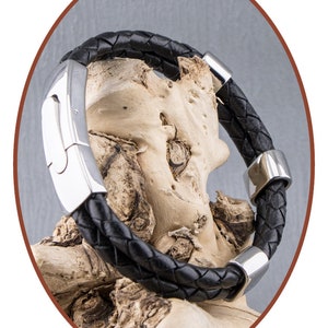 K&ouml;nnte beinhalten: Ein schwarzes Lederarmband mit einem silbernen Verschluss und silbernen Akzenten. Das Armband ist geflochten und hat eine polierte Oberfl&auml;che.