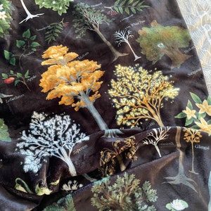 May include: A black fabric with a variety of trees and plants printed on it. The trees and plants are in shades of green, yellow, and white. The fabric has a velvety texture.