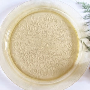 May include: A large, round, yellow glass serving tray with a raised, embossed floral design. The tray has a scalloped edge.
