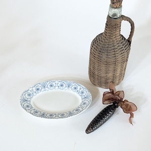 May include: An oval white serving platter with a blue floral design, a brown wicker-covered bottle with a cork stopper, and a dark brown decorative item with a brown ribbon.