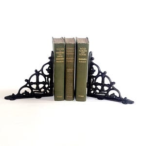 May include: Two black cast iron bookends with an ornate scrollwork design supporting three green hardcover books. The books are titled Field Book of American Trees and Shrubs, Field Book of American Wild Flowers, and Wild Flowers and Ferns by Putnam.