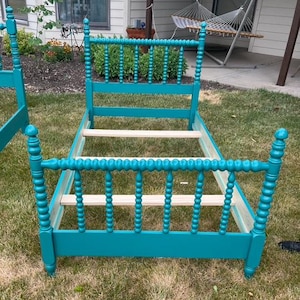 May include: A teal-colored bed frame with a spindle design. The headboard and footboard feature vertical spindles and rounded posts. The bed frame is made of wood and is painted in a bright teal color.