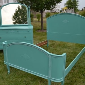May include: A teal blue bedroom set with a dresser and a headboard. The dresser has three drawers and a mirror. The headboard has a curved top and a decorative design.