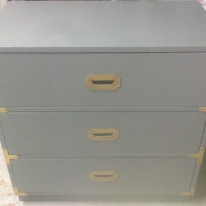 May include: A gray three-drawer dresser with brass hardware and a simple design.