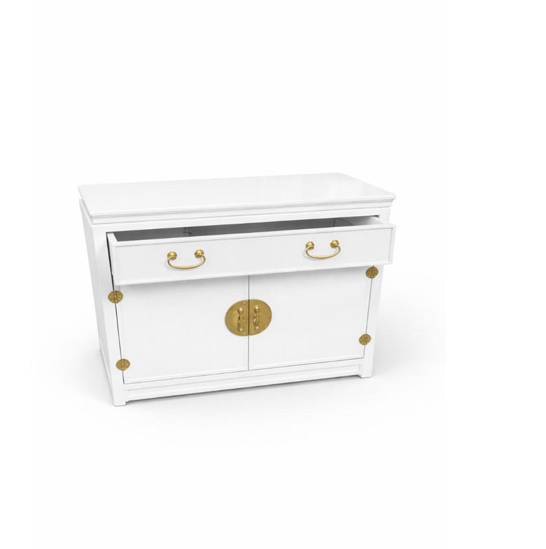 May include: A white cabinet with a rectangular top and two doors. The cabinet has a drawer that is partially open. The hardware is gold-colored, including the drawer pulls and the door handles.