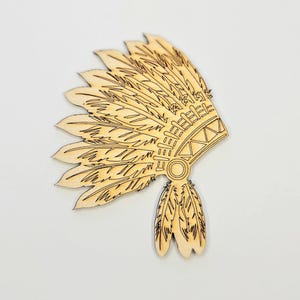 May include: A wooden Native American headdress cutout. The headdress features a fan of feathers, intricate geometric designs, and a central circular element. The natural wood color and detailed laser-cut lines give it a rustic appearance.