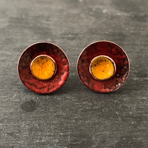 Puede incluir: Un par de pequeños pendientes redondos con un diseño de esmalte rojo y naranja. Los pendientes tienen una superficie texturizada y un centro circular elevado.