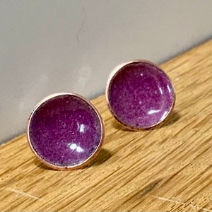 Könnte beinhalten: Ein Paar kleine, runde Ohrringe mit einer violetten Emaille-Oberfläche. Die Ohrringe haben eine Roségold-Tönung.