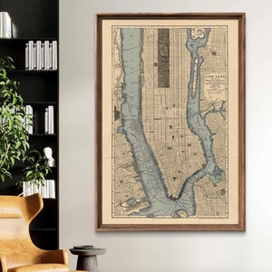 May include: A framed vintage map of New York City, featuring a detailed street grid and waterways in shades of blue and beige. The map is encased in a dark wooden frame, displayed on a white wall. The map is labeled "New York".