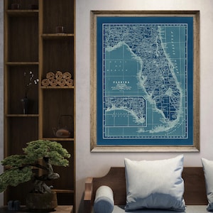 May include: A framed vintage map of Florida, featuring a detailed depiction of the state in shades of blue and white. The map is enclosed in a wooden frame, adding a classic touch. The word "Florida" is visible on the map.