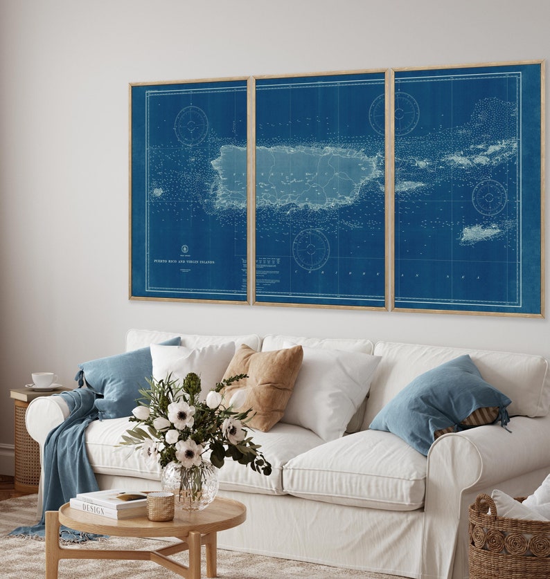 May include: A three-piece set of vintage nautical charts of Puerto Rico and Virgin Islands, printed on blue paper with white lines and text. The charts are framed in natural wood frames and displayed on a white sofa with blue and brown throw pillows.