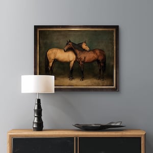 May include: A framed artwork depicting two horses. One horse is a light tan color, and the other is a rich brown. They stand close together, their bodies touching. The artwork has a dark, ornate frame.
