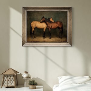 May include: A framed painting depicts two horses, one tan and one brown, standing close together. The horses are set against a dark green background, and the frame is a light, neutral color. The artwork is displayed on a light-colored wall.