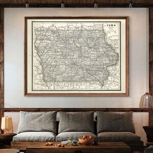 May include: A framed vintage map of Iowa, featuring intricate details of roads, cities, and geographical features. The map is printed in black and white and is set within a dark wooden frame. The word "IOWA" is printed at the top right corner.