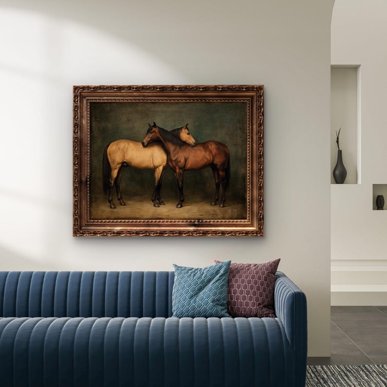 May include: A framed painting depicts two horses, one tan and one brown, standing close together. The artwork has a dark background and is encased in a decorative, ornate brown frame. The painting hangs above a blue sofa with patterned throw pillows.
